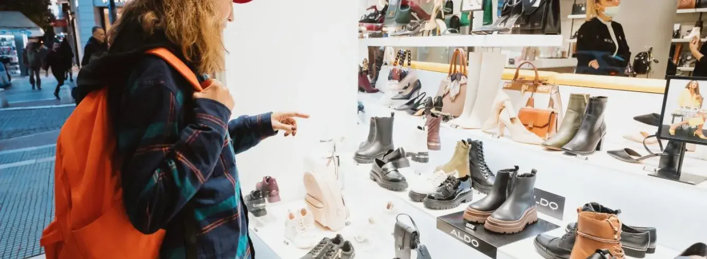 person wearing a red backpack and flannel window shopping for shoes